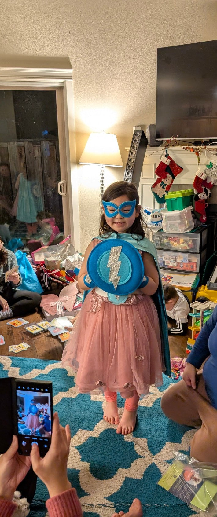 Girl in superhero costume with cape and mask surrounded by toys and furniture. Creativeapes.com was the favorite Christmas gift