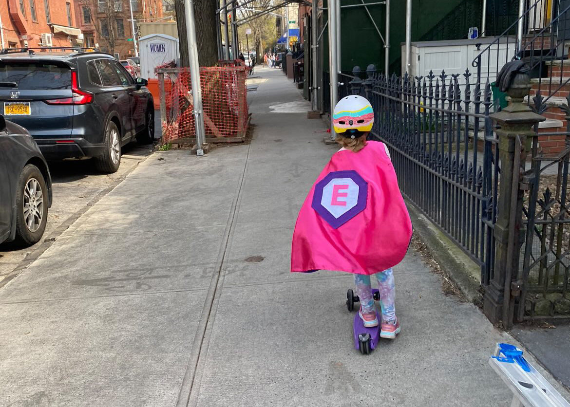 Girl in New York wearing pink satin cape made by Creative Capes on her scooter ready to save the day