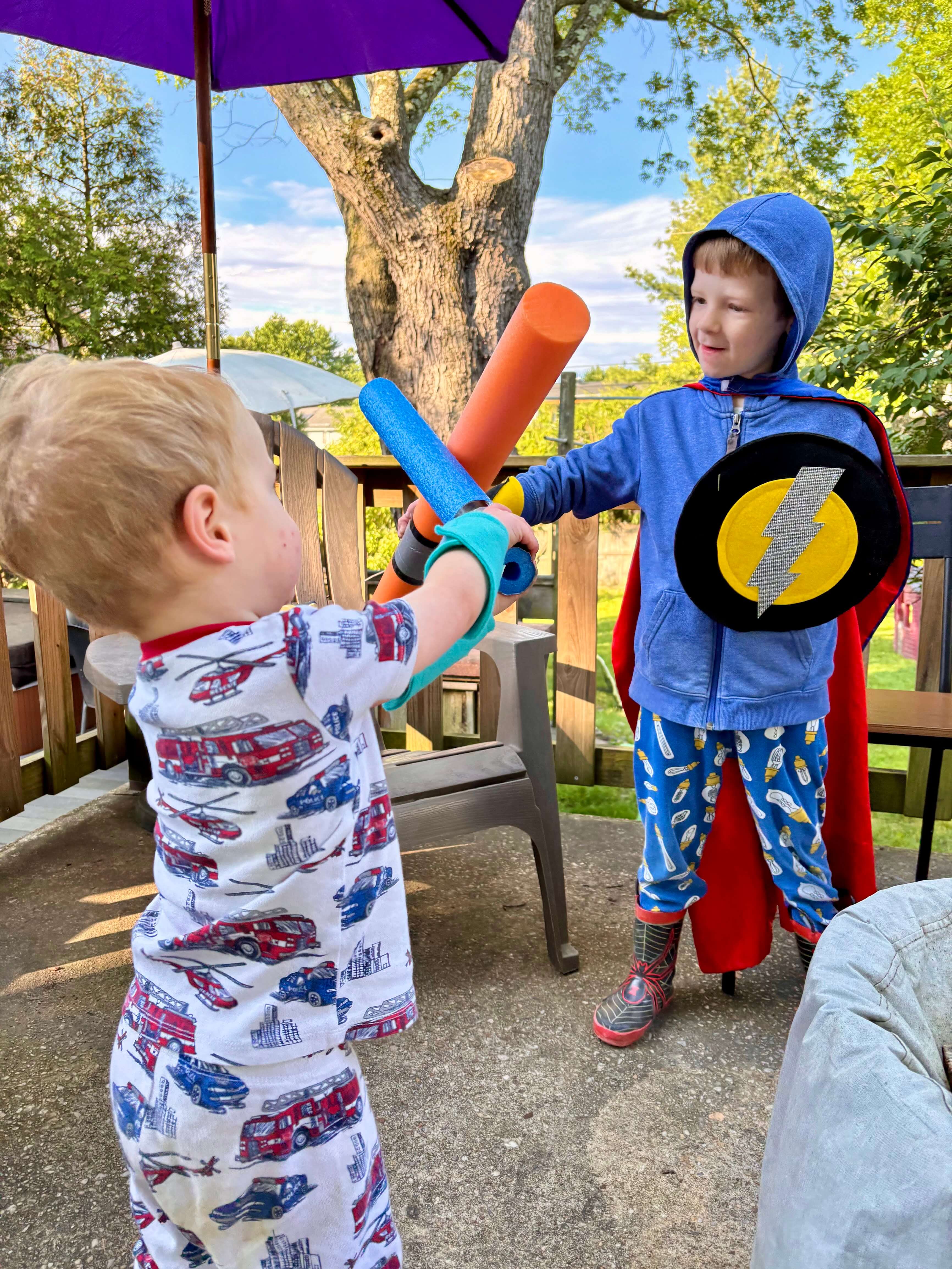 Two children playing outdoors with superhero toy shields and arm bands by Creative Capes. Open-ended play inspires creative minds at a young age