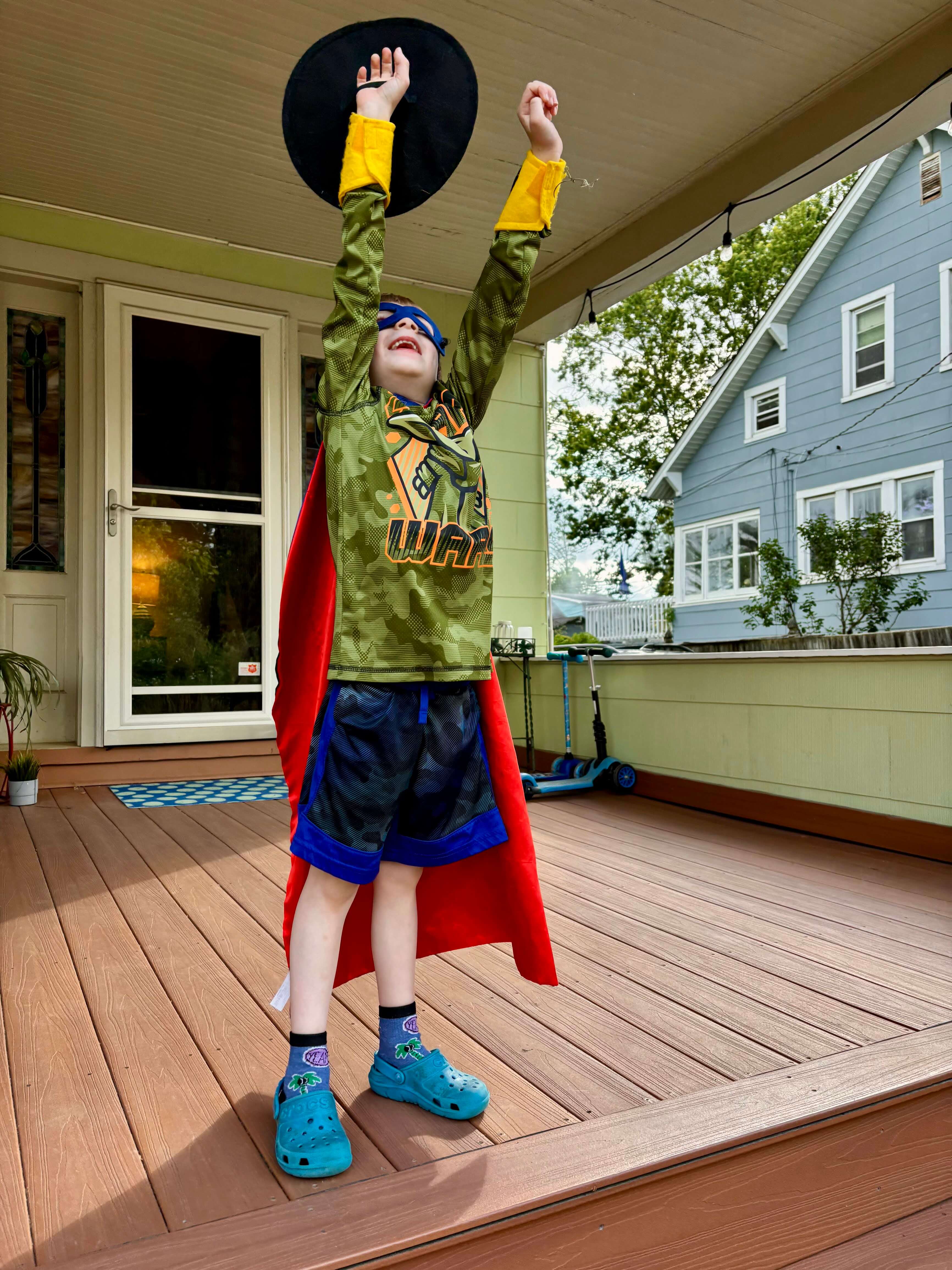 Boy role playing as a superhero using Creative Capes black felt shield and yellow arm bands
