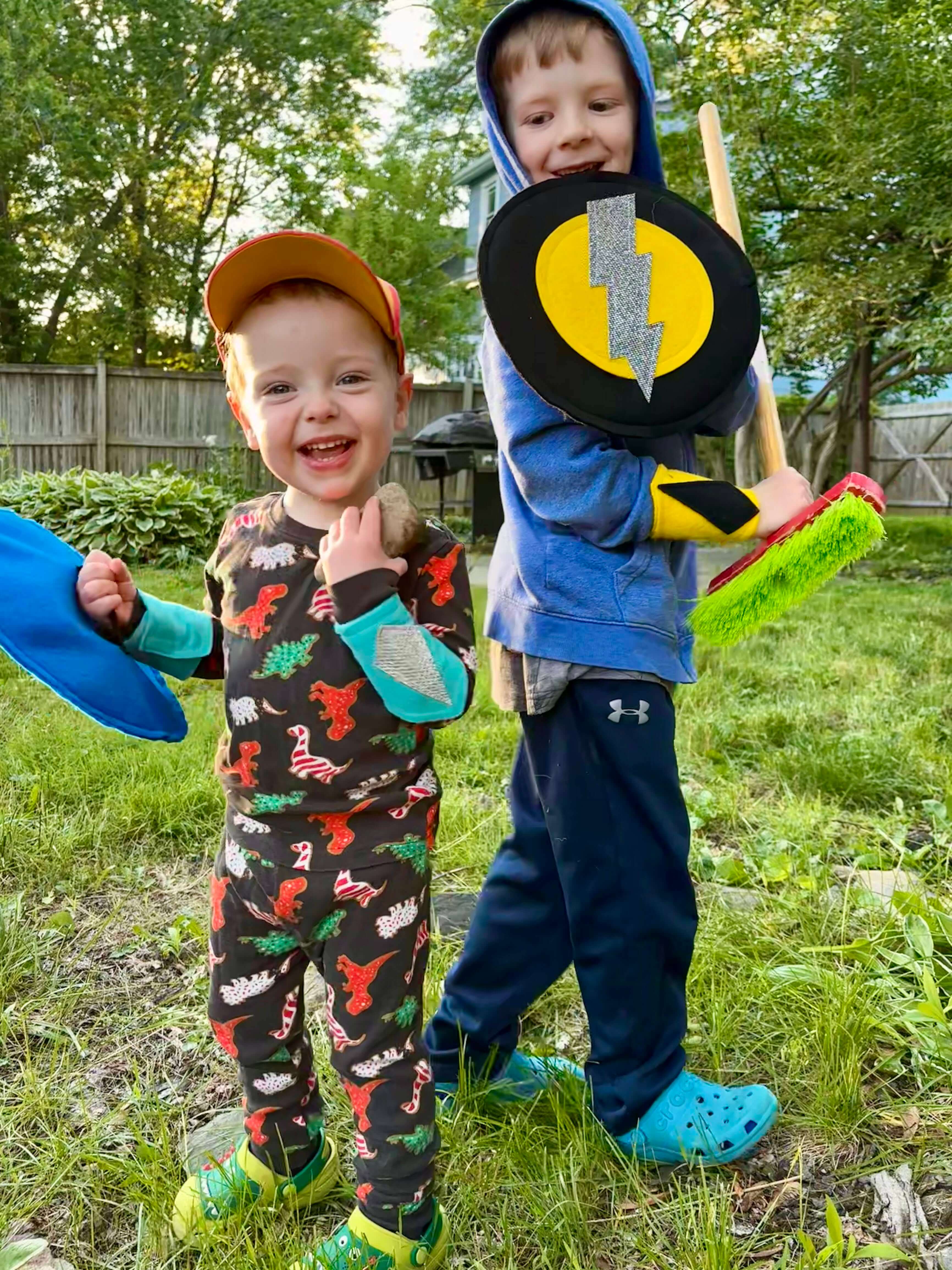 Two children playing pretend outdoors with superhero felt shields and felt arm bands created by CreativeCapes.com in the USA for creative play