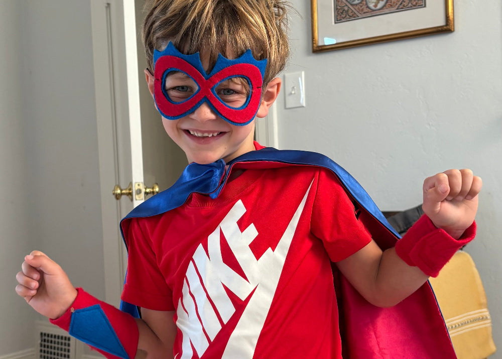Boy in superhero costume with red cape, arm bands and spike shaped mask