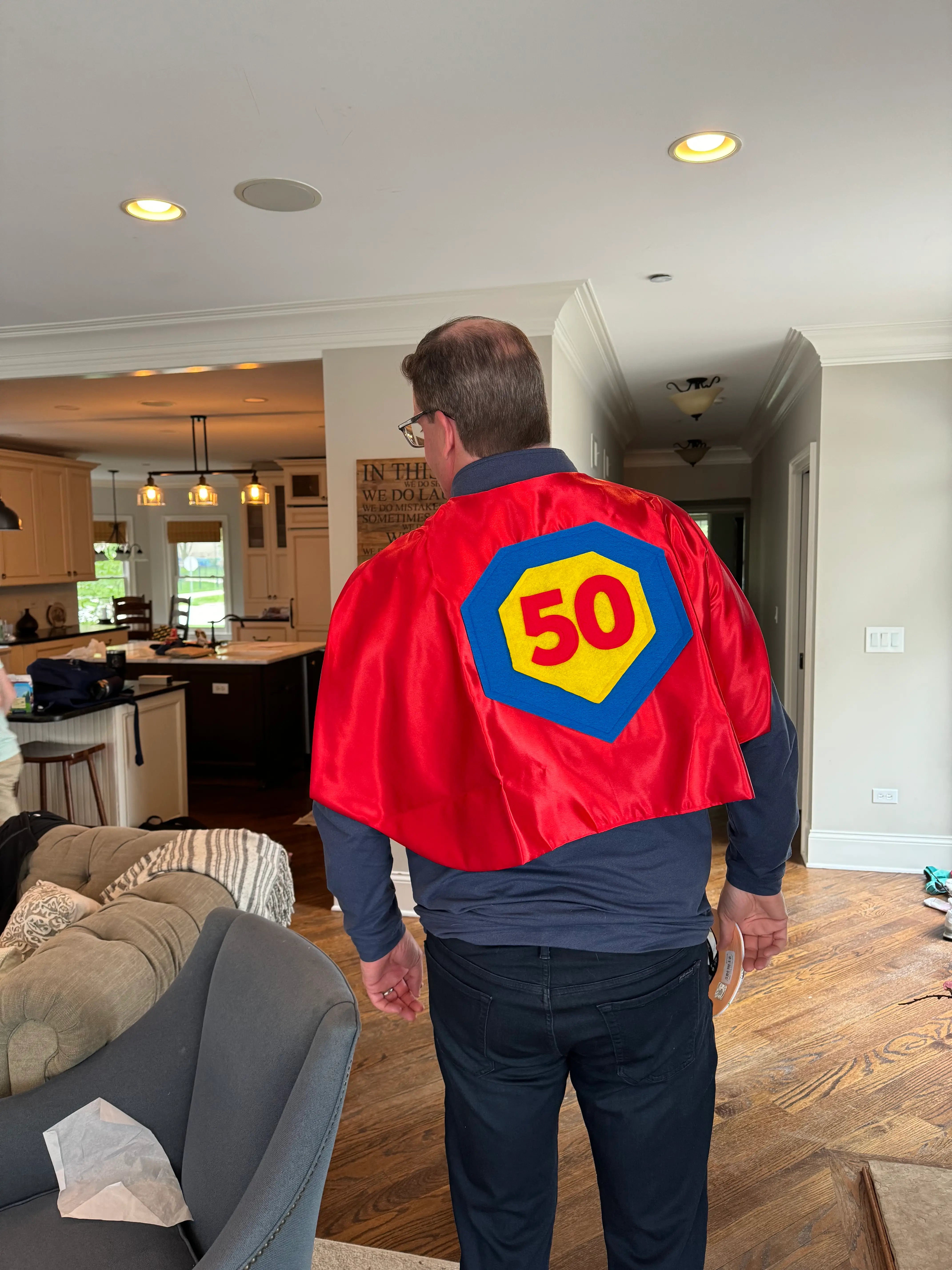Man wearing an adult red superhero cape with a '50' emblem that was made in the USA by Creative Capes, a small business.