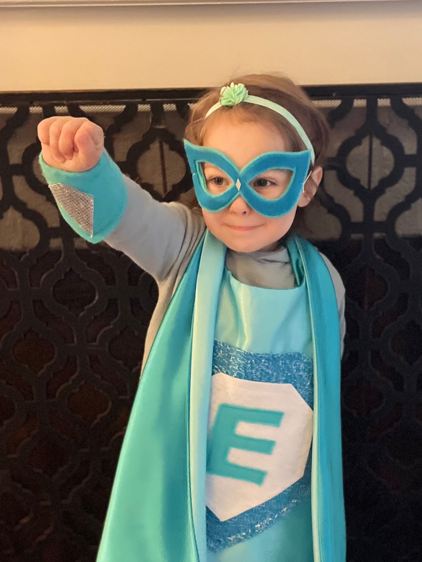 Girl in superhero costume with blue mask and cape, concentrating on becoming her own super hero, pretend play is the best