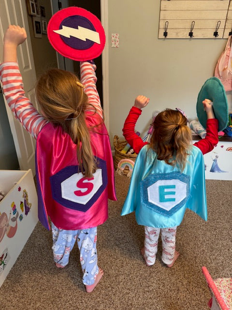 girls in playroom with arms up feeling strong as the become their own superhero thanks to Creative Capes