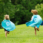 girls running in aqua satin super hero capes that are handmade by Creative Capes. Building strong girls through positive play