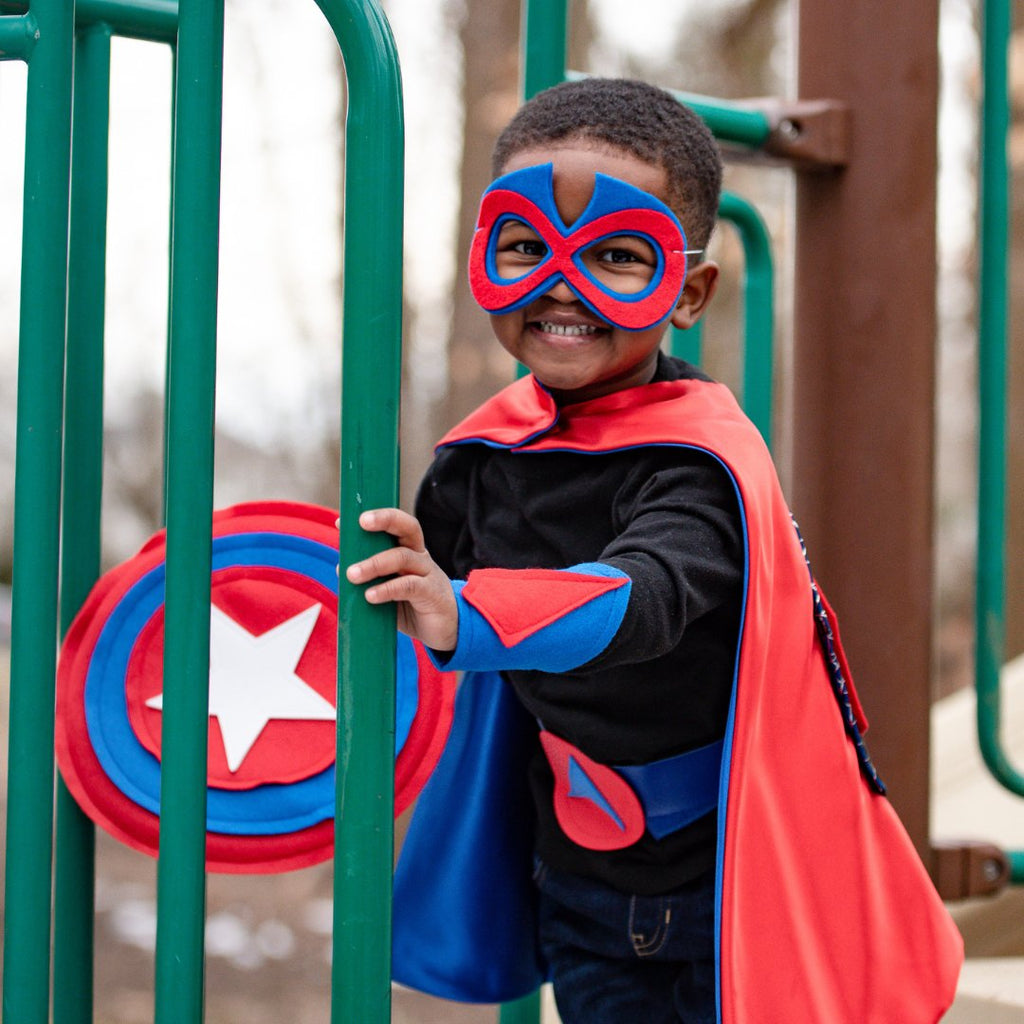 preschooler playing in dress-up red spidey cape costume and shield
