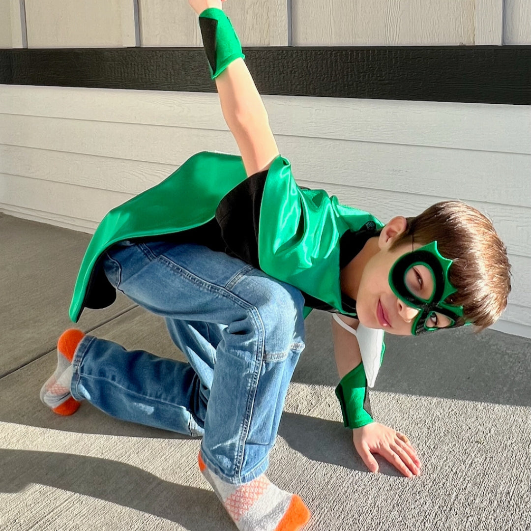boy in positive affirmation green and black personalized superhero costume set,  dress-up costume kit - lined satin cape, shield, mask, belt, and wrist cuffs. Handmade by Creative Capes in USA to inspire imaginative play and confidence, activity for healthy childhood.