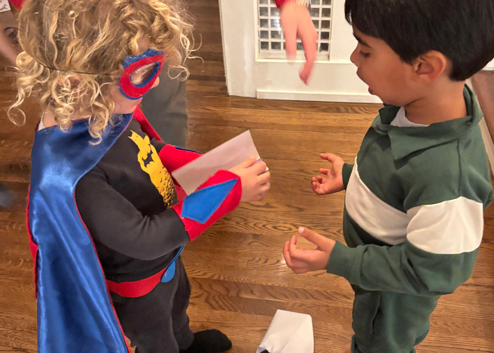 Child in blue satin superhero costume interacting with another child 