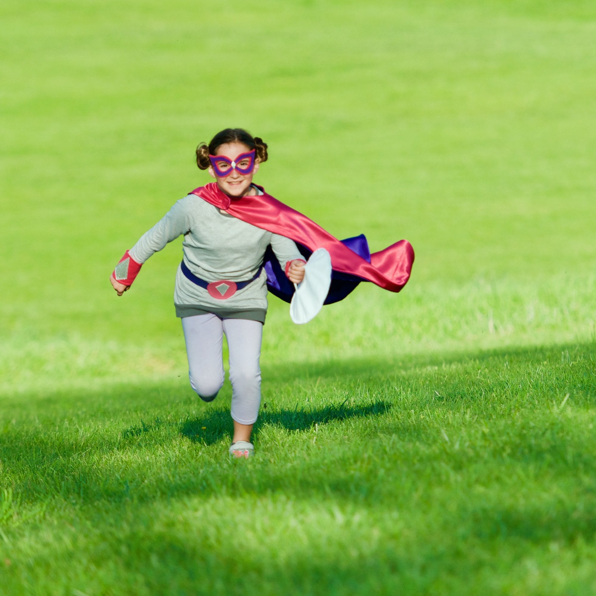 girl feeling proud and strong in her purple and pink personalized superhero costume set, featuring the child's first initial on the super hero cape. The dress-up costume kit includes a lined satin cape, shield, mask, belt, and wrist cuffs. Handmade by Creative Capes in USA to inspire imaginative play and confidence. Play without screens creates a healthy childhood.