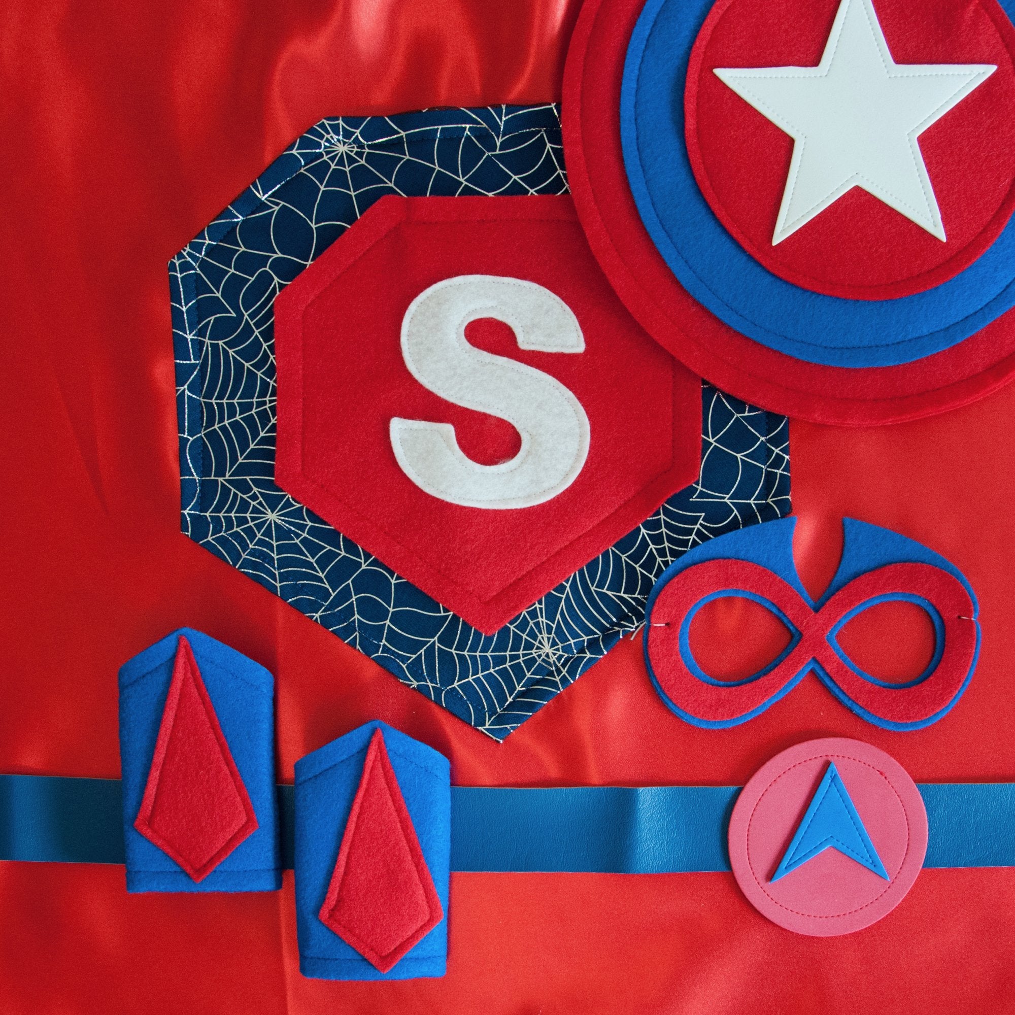 Red and blue cape, personalized superhero costume set for kids, child's first initial cape with a spiderweb design, shield, mask, belt, and wrist cuffs. Handmade by Creative Capes, toy to inspire imaginative play and confidence, Spiderman fan