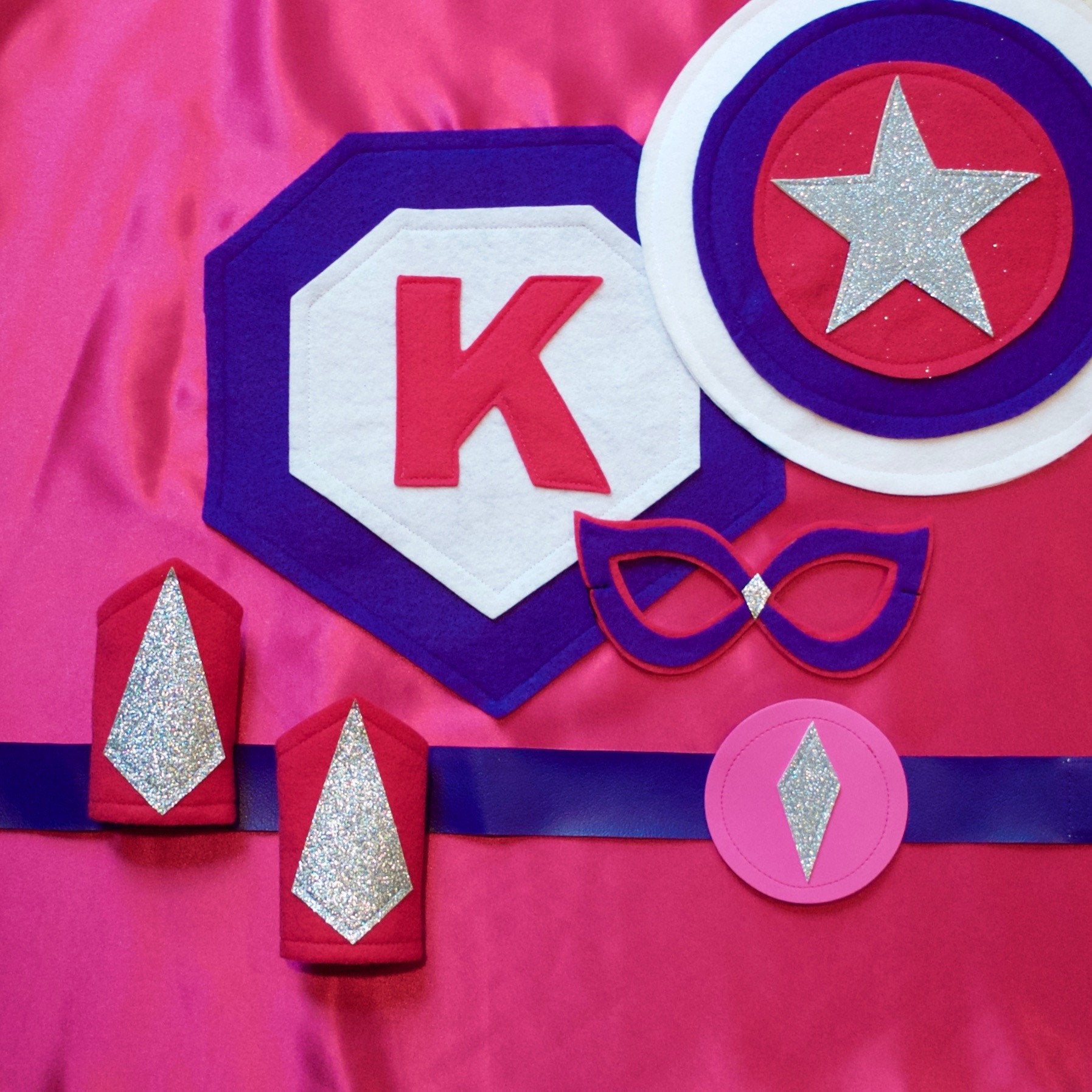 purple and pink personalized superhero costume set, cape with child's first initial, dress-up costume kit - lined satin cape, shield, mask, belt, and wrist cuffs, handmade by Creative Capes in USA, play activity to inspire imaginative play and confidence, healthy alternative to screen time
