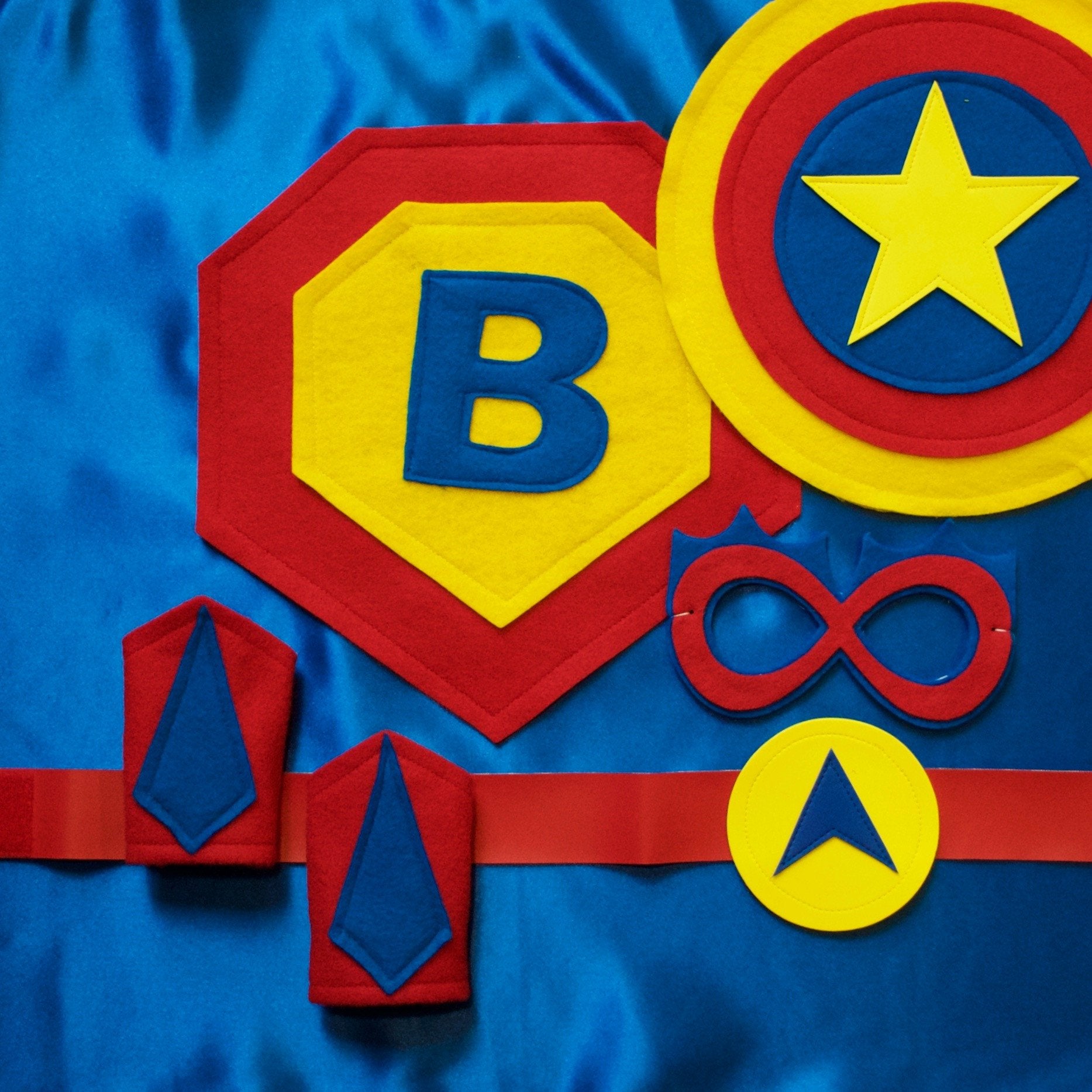 personalized blue, red and yellow superhero costume set, featuring the child's first initial on the super hero cape, quality dress-up costume kit includes a lined satin cape, shield, mask, belt, and wrist cuffs, handmade by Creative Capes in USA to inspire imaginative play and confidence. Play without screens creates a healthy childhood.