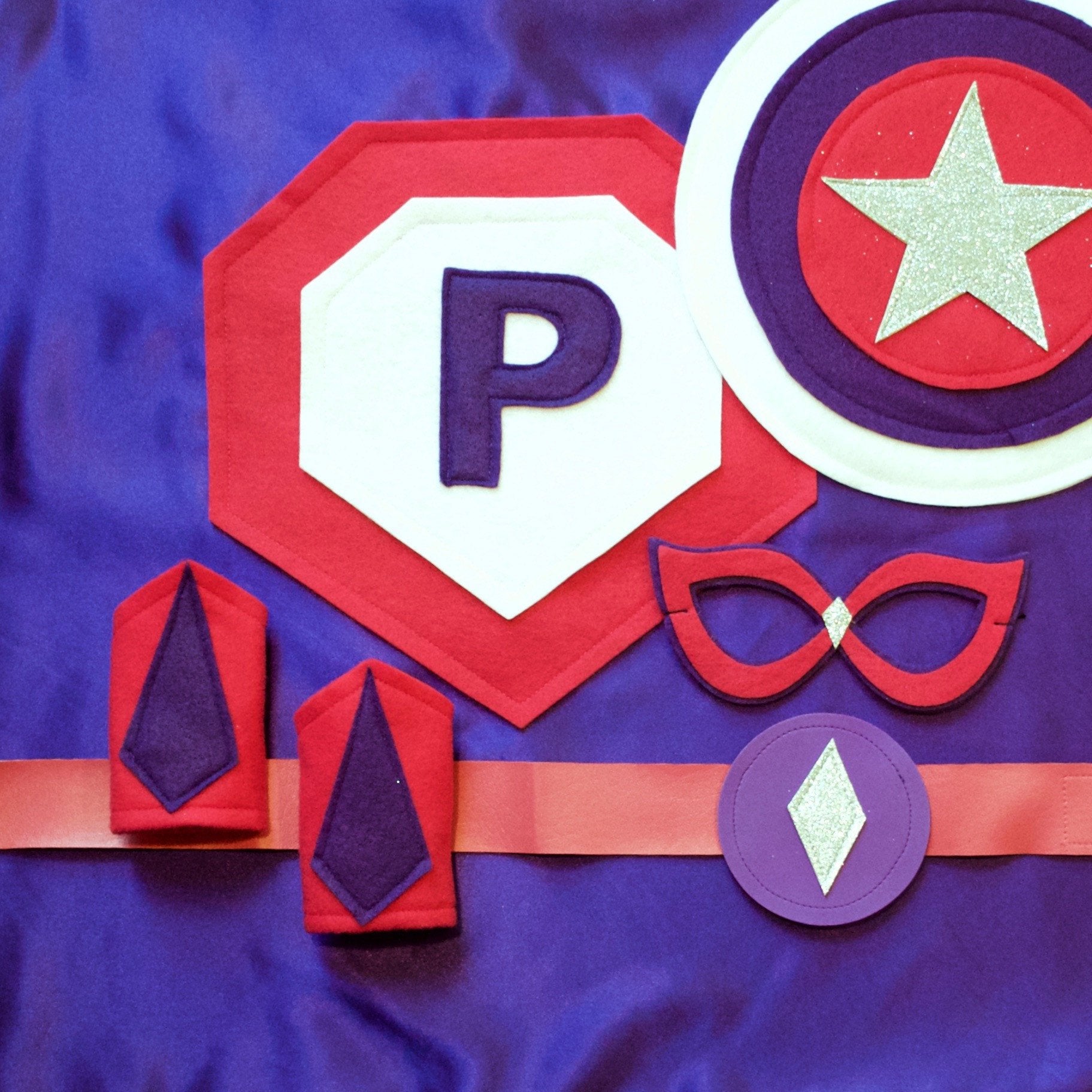 purple and pink personalized superhero costume set, cape with child's first initial, dress-up costume kit - lined satin cape, shield, mask, belt, and wrist cuffs, handmade by Creative Capes in USA, play activity to inspire imaginative play and confidence, healthy alternative to screen time